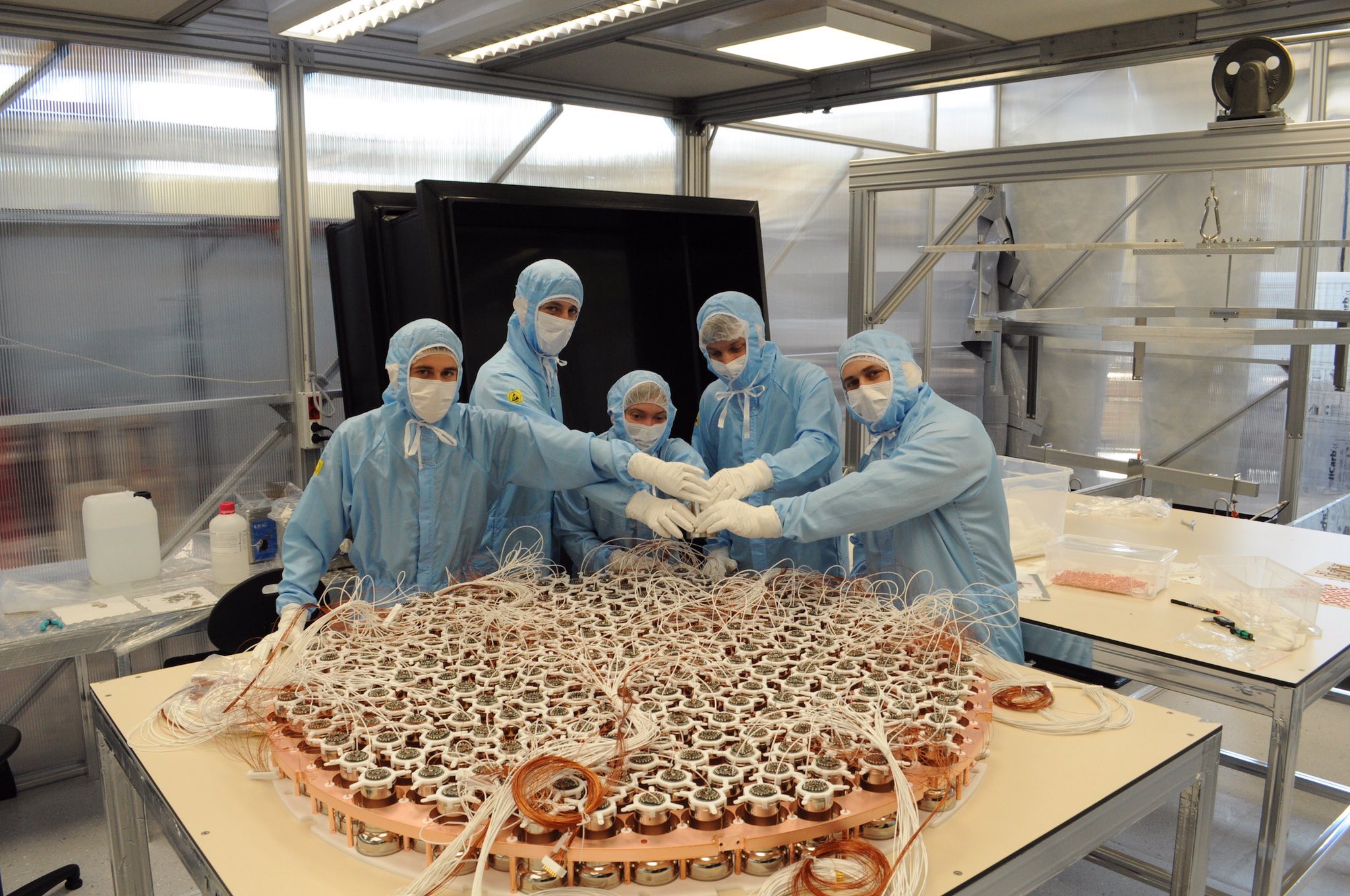 Array of photomultipliers with cables. Five cleanroom-suited physicists are standing behind the array